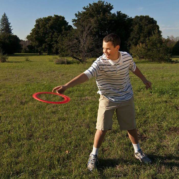 Aerobie - Junge wirft orangen Ring auf Wiese