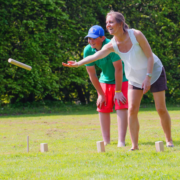 Aerobie - Junge und Frau spielen auf der Wiese Spiel mit Holzfiguren